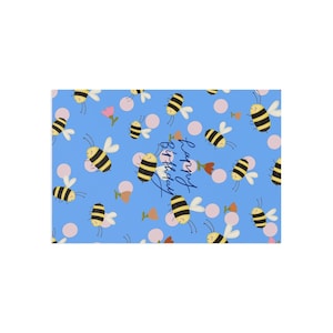 Könnte beinhalten: Ein rechteckiges Blatt Geschenkpapier mit hellblauem Hintergrund und einem wiederkehrenden Muster aus gezeichneten Bienen, kleinen rosa Kreisen und winzigen orangefarbenen Blumen. Der Text "Happy Birthday" ist in dunkelblauer Schreibschrift.