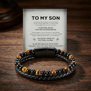 Peut inclure: Un bracelet de perles noires et dorées avec un fermoir magnétique, accompagné d'une carte avec l'inscription "TO MY SON". Le bracelet est composé de perles noires et dorées et d'un bracelet en cuir tressé. La carte contient un message de soutien.