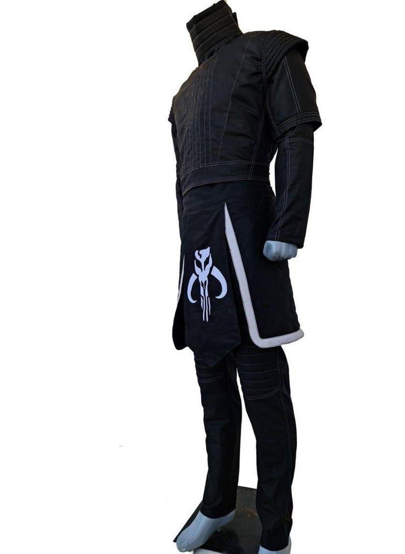 May include: Black costume with a high collar, short sleeves, and a skirt-like panel. The costume features white trim and a white emblem on the front. The pants are black with stitched details. The costume is displayed on a mannequin.