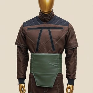 Puede incluir: Traje futurista marr&oacute;n y negro sobre un maniqu&iacute;. El traje presenta un cuello alto, mangas cortas y un cintur&oacute;n verde. El dise&ntilde;o incluye detalles en negro y costuras blancas.