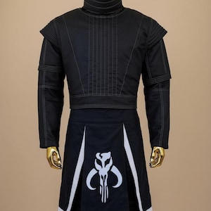 May include: Black costume with white stitching and accents. The outfit includes a high-collared jacket with shoulder pads and a skirt-like bottom with a white graphic. The costume is displayed on a gold mannequin.