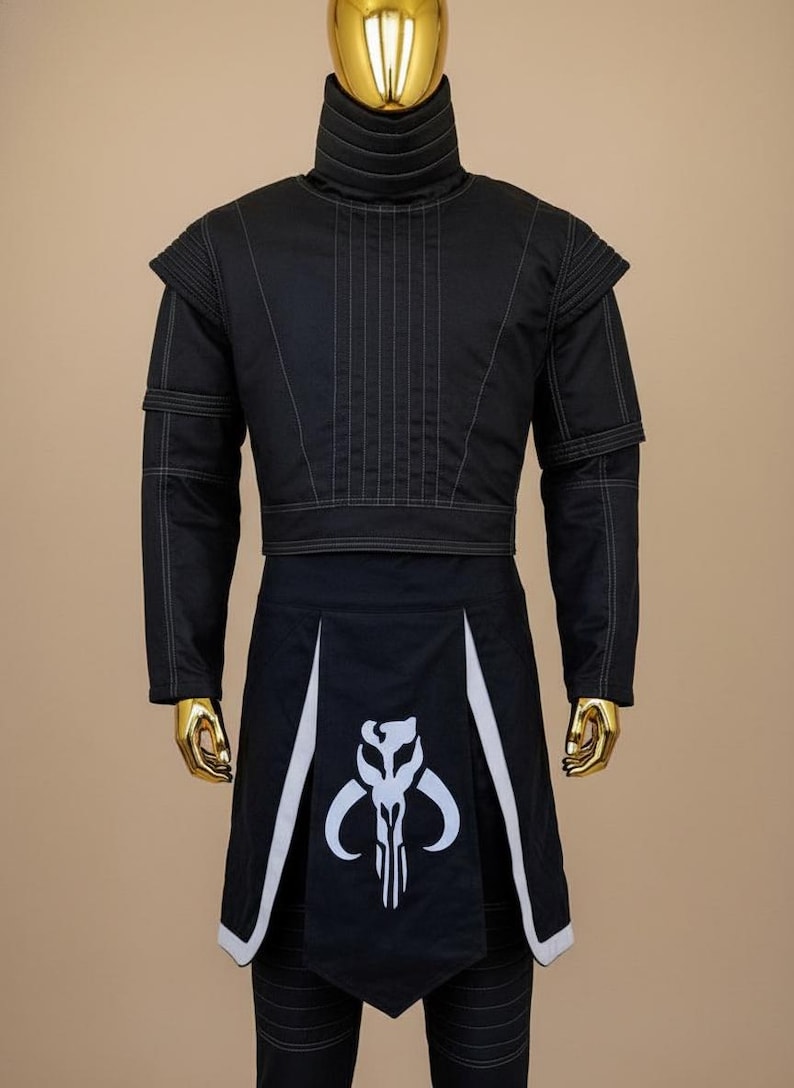 May include: Black costume with white stitching and accents. The outfit includes a high-collared jacket with shoulder pads and a skirt-like bottom with a white graphic. The costume is displayed on a gold mannequin.