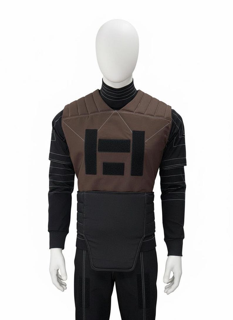 May include: Brown and black tactical vest with a geometric design on a mannequin. The vest has a padded brown front with black rectangular accents and a black lower section. The mannequin is wearing a black long-sleeved shirt and pants.