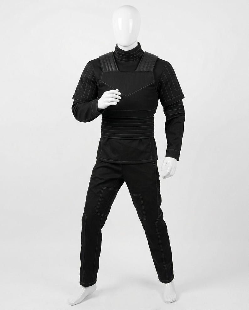 Pode incluir: Um traje preto exibido em um manequim. O traje inclui uma camisa de manga comprida com gola alta, cal&ccedil;as e uma pe&ccedil;a semelhante a um colete com detalhes nos ombros. A costura &eacute; vis&iacute;vel, e o design geral &eacute; elegante e moderno.
