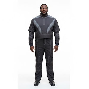 May include: A dark gray jumpsuit with a short-sleeved top and long pants. The top has gray accents and a high collar. The pants have white stitching and pockets. The sleeves have a geometric pattern. The person is wearing black shoes.