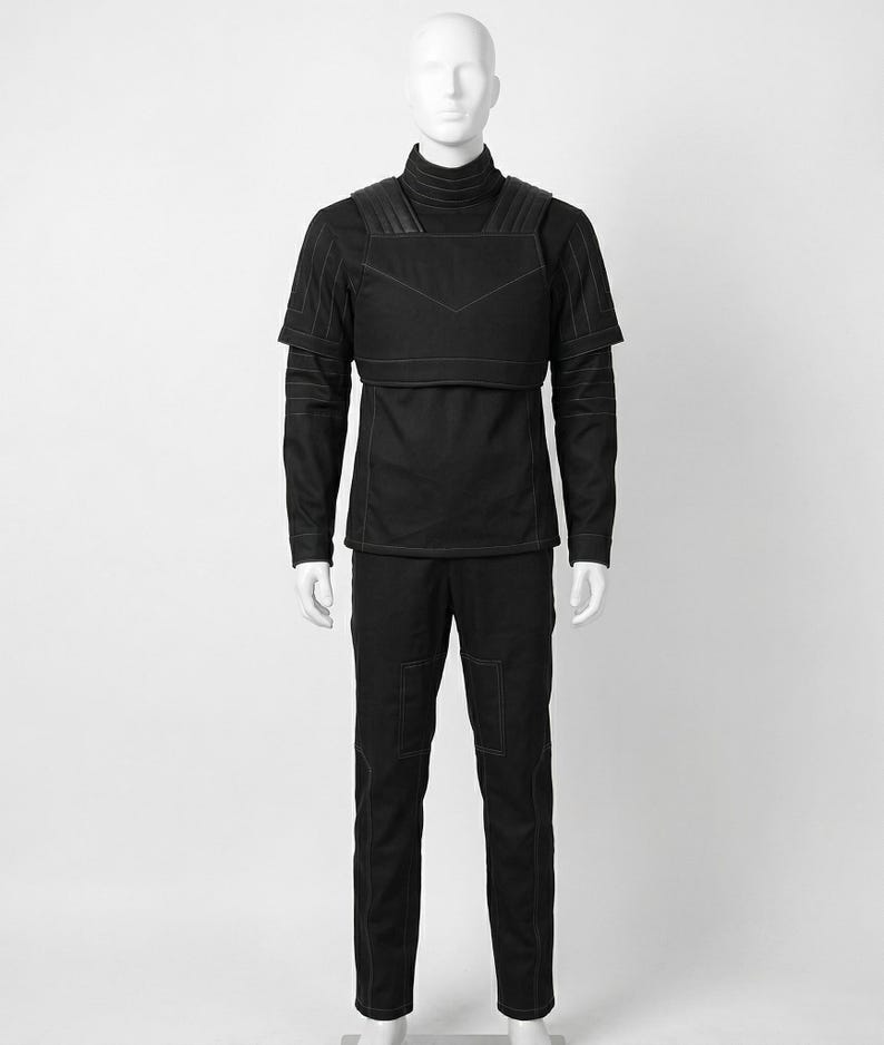 Pode incluir: Roupa t&aacute;tica preta exibida em um manequim. O conjunto inclui uma camisa de gola alta, um colete com detalhes em couro e cal&ccedil;as combinando. As costuras e os bolsos s&atilde;o detalhados com costuras brancas. A roupa &eacute; projetada para uma est&eacute;tica elegante e moderna.