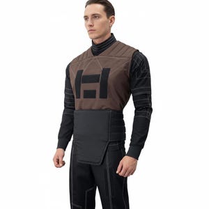 May include: A brown quilted vest with a black rectangular design on the front. The vest is worn over a black long-sleeved shirt and paired with black pants. White stitching accents the seams of the vest and shirt.