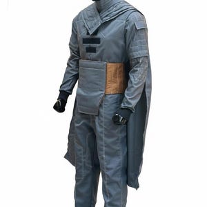 May include: A gray costume displayed on a mannequin. The outfit includes a long-sleeved top with geometric accents, matching pants, and a brown belt. The costume has a cape-like element and is likely for cosplay or a themed event.