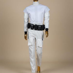 May include: A futuristic white outfit on a mannequin. The ensemble includes a high-collared top with blue stitching, matching trousers with cargo pockets, and a black belt with pouches. The mannequin has a gold head and hands.
