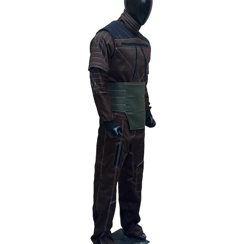 Puede incluir: Mono marr&oacute;n con costuras en contraste y cintur&oacute;n verde oscuro. El atuendo presenta un cuello alto, detalles en los hombros y guantes negros. El maniqu&iacute; lleva un casco negro.