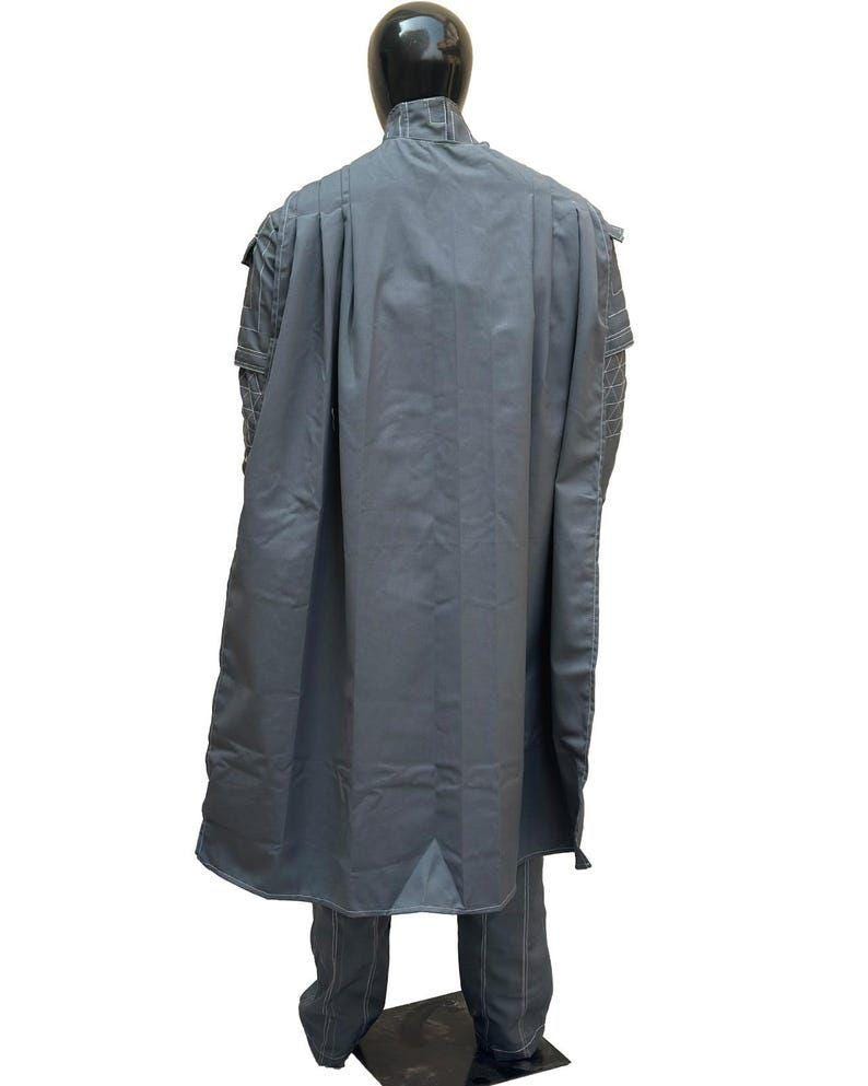May include: A gray costume with a cape, jacket, and pants. The cape drapes down the back, and the jacket has detailed stitching on the shoulders. The pants have white stitching. The outfit is displayed on a black mannequin.