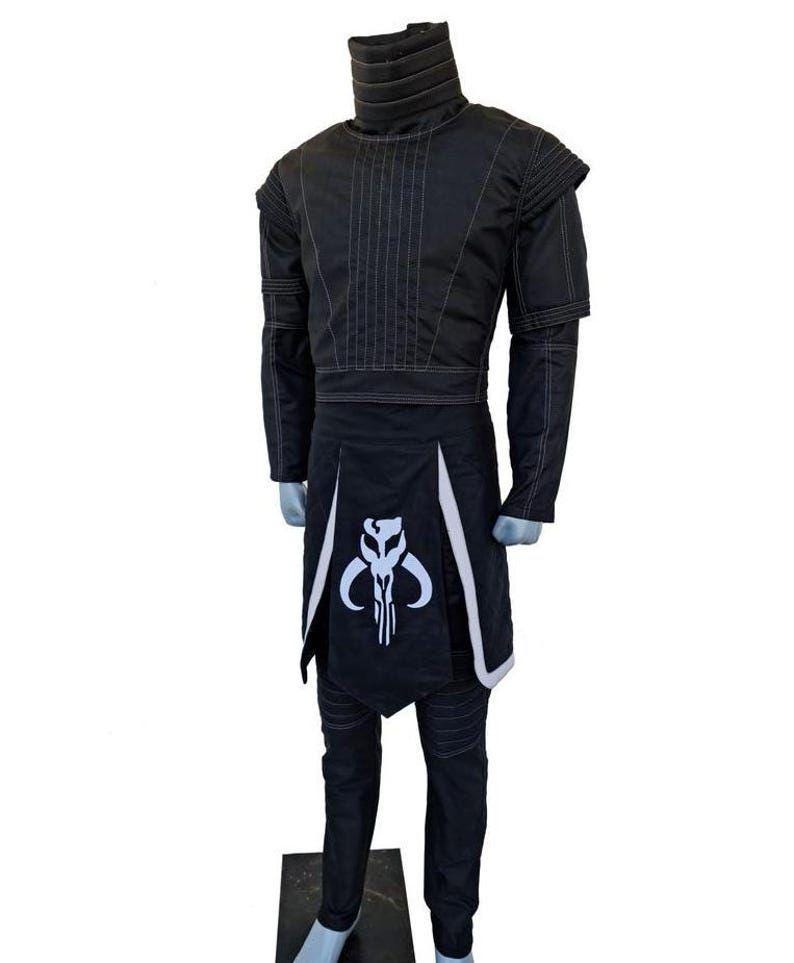 May include: Black costume with white accents, displayed on a mannequin. The outfit includes a high-collared jacket, pants, and a skirt-like piece with a white skull emblem. The jacket has vertical stitching and the pants have horizontal stitching.