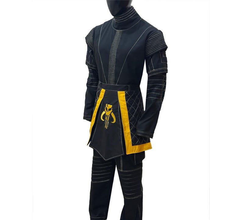 May include: Black costume with yellow detailing, including a high collar and a unique emblem. The outfit comprises a long-sleeved top, trousers, and an apron-style element. The costume features white stitching.