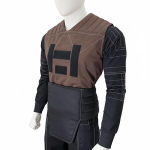 May include: A brown and black tactical vest and pants set displayed on a mannequin. The vest features a padded design with a large black logo. The long-sleeved shirt and pants are black with white stitching.