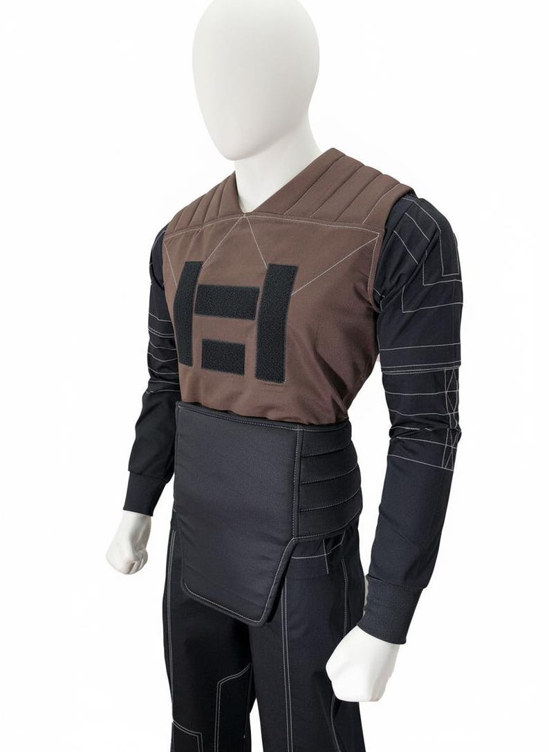 May include: A brown and black tactical vest and pants set displayed on a mannequin. The vest features a padded design with a large black logo. The long-sleeved shirt and pants are black with white stitching.