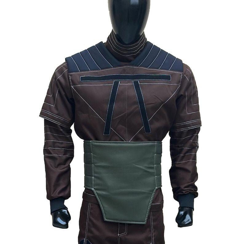 Puede incluir: Un disfraz marr&oacute;n con cuello alto, detalles en los hombros azul oscuro y ribetes negros. El disfraz presenta un cintur&oacute;n verde y pu&ntilde;os negros. El atuendo se exhibe en un maniqu&iacute;.