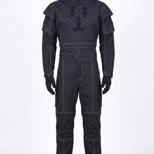 Puede incluir: Mono azul marino oscuro con detalles de costuras blancas. El atuendo incluye un cuello alto, detalles en los hombros y bolsillos cargo en los pantalones. Guantes y botas negras completan el conjunto. El mono se exhibe en un maniqu&iacute;.