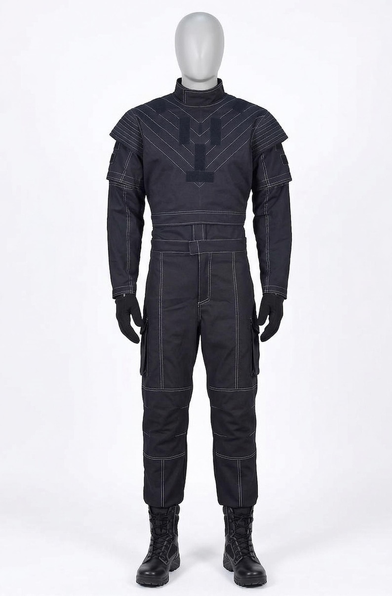 Puede incluir: Mono azul marino oscuro con detalles de costuras blancas. El atuendo incluye un cuello alto, detalles en los hombros y bolsillos cargo en los pantalones. Guantes y botas negras completan el conjunto. El mono se exhibe en un maniqu&iacute;.