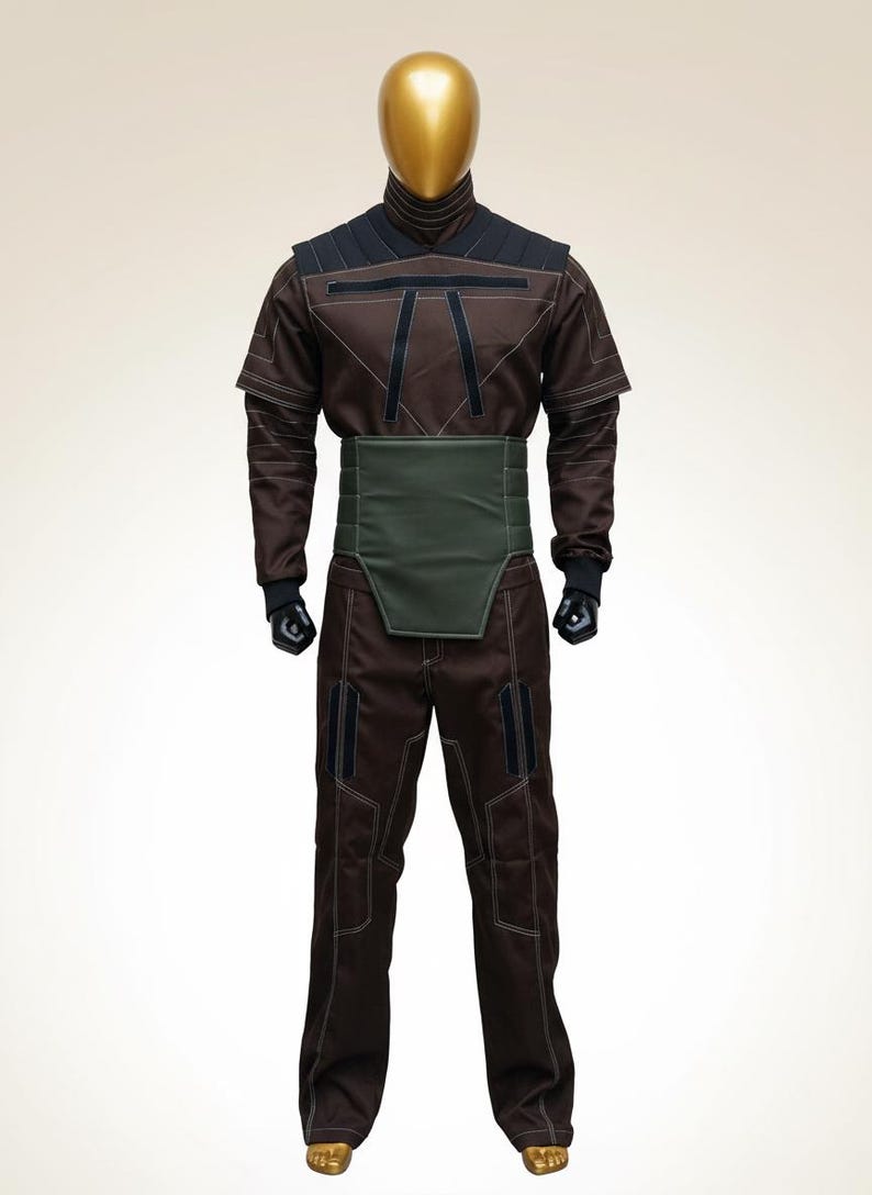 Puede incluir: Mono marr&oacute;n con detalles negros y una faja verde, exhibido en un maniqu&iacute; con cabeza dorada. El atuendo tiene un cuello alto y costuras visibles. Los pantalones tienen bolsillos.