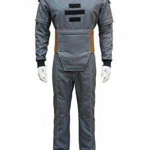 May include: A gray jumpsuit with a high collar, featuring a brown belt and black accents. The suit has white stitching details and is displayed on a mannequin. The overall design suggests a futuristic or sci-fi theme.