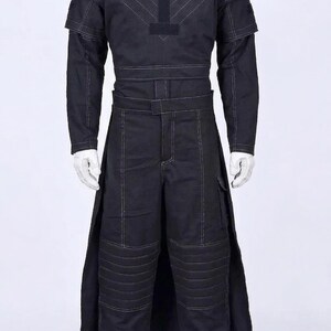 Puede incluir: Traje negro con costuras blancas, que incluye una parte superior de manga larga con detalles en los hombros y cintura con cintur&oacute;n, adem&aacute;s de pantalones con bolsillos de carga y acolchado en las rodillas. Botas blancas completan el conjunto. El traje tiene un dise&ntilde;o futurista.