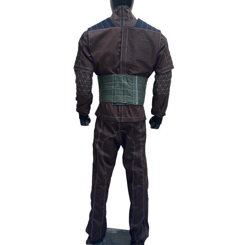 Puede incluir: Mono marr&oacute;n con cintur&oacute;n verde y detalles negros. El traje tiene costuras blancas y patrones geom&eacute;tricos en las mangas. Parches azul oscuro en los hombros.