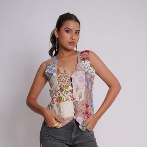Può includere: Un gilet senza maniche con un motivo floreale patchwork multicolore e chiusura frontale a bottoni, abbinato a jeans in denim grigio antracite con pannelli in tessuto patchwork lungo le cuciture laterali e orlo sfrangiato alle caviglie.