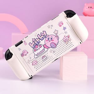 May include: White Nintendo Switch Joy-Con controller case featuring a colorful Kirby design. The case has a cartoon illustration of Kirby, stars, and cake. The controller has black accents and a dotted pattern.