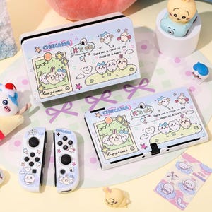 Peut inclure: Un étui et un ensemble de manettes Nintendo Switch bleu clair avec un design de dessin animé. L'étui et les manettes présentent des illustrations de lapins, de nuages et le texte "CHIIKAWA" et "it's ok". L'ensemble comprend un étui, deux manettes et des autocollants.