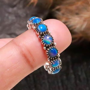 May include: A silver ring featuring a series of vibrant blue opal stones. The ring's band has a detailed, ornate design. The opals are round and set closely together, creating a continuous line of color. The ring is a piece of jewelry.