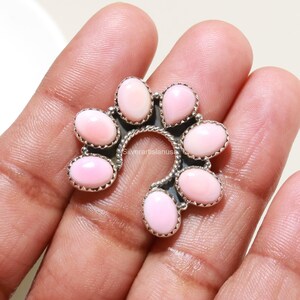 Peut inclure: Une broche en argent en forme de fer à cheval ornée de sept pierres cabochons rose clair, lisses et ovales, serties dans des chatons festonnés. La monture en métal présente une texture torsadée sur le bord intérieur et le texte silverartisanusa.