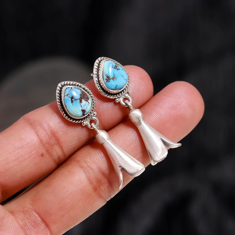 Peut inclure: Une paire de boucles d'oreilles en argent avec des pierres turquoise en forme de goutte d'eau et des veines marron. Les pierres sont serties dans un cadre perl&eacute;. Les boucles d'oreilles ont un design floral.