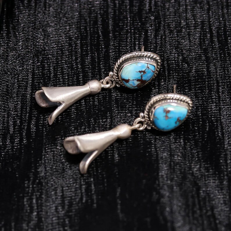 Peut inclure: Paire de boucles d'oreilles argent&eacute;es avec des pierres turquoise. Les boucles d'oreilles ont une forme de goutte d'eau avec un motif floral en bas. Les pierres turquoise sont ovales et serties dans une lunette argent&eacute;e.