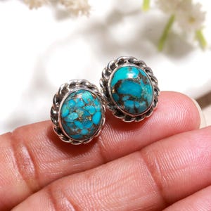 May include: A pair of oval stud earrings featuring bright turquoise stones with dark brown matrix patterns. Each stone is set in a polished silver bezel with a twisted rope border design. The text SilverArtisanusa is visible on the stones.