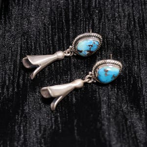 Peut inclure: Paire de boucles d'oreilles argent&eacute;es avec des pierres turquoise. Les boucles d'oreilles ont une forme de goutte d'eau avec un motif floral en bas. Les pierres turquoise sont ovales et serties dans une lunette argent&eacute;e.