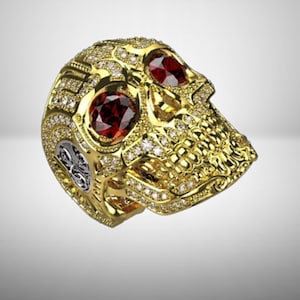 May include: A gold skull ring with red gemstone eyes and encrusted with small diamonds. The ring has intricate detailing and a silver accent on the side.