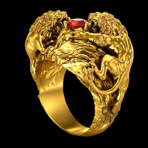 Könnte beinhalten: Goldfarbener Ring mit zwei detaillierten Löwenfiguren, die sich gegenüberstehen, mit einem roten Edelstein dazwischen. Der Ring hat ein strukturiertes Design und ein breites Band, vor schwarzem Hintergrund.