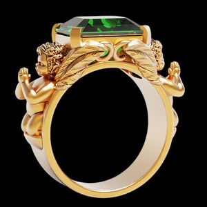 Peut inclure: Bague en or orn&eacute;e d'une grande pierre verte taill&eacute;e en &eacute;meraude. Deux ch&eacute;rubins encadrent la gemme, avec des d&eacute;tails de plumes. La bague pr&eacute;sente un design bicolore, avec un ext&eacute;rieur dor&eacute; et un int&eacute;rieur argent&eacute;.