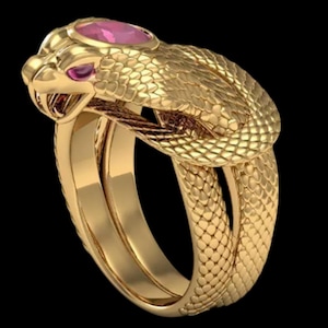 May include: A gold-colored ring in the shape of a snake, with a textured, scaled body. The snake's head features a pink gemstone eye and a larger pink gemstone on the head. The ring has a double band design.