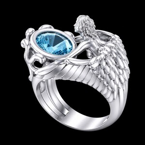 May include: A silver-toned ring featuring a central oval-cut light blue gemstone. The band is sculpted into the shape of a winged figure with detailed feathers extending along the sides, cradling the stone in an ornate, decorative setting.