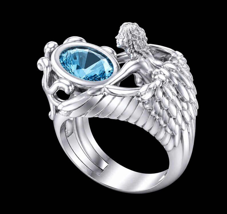 May include: A silver-toned ring featuring a central oval-cut light blue gemstone. The band is sculpted into the shape of a winged figure with detailed feathers extending along the sides, cradling the stone in an ornate, decorative setting.