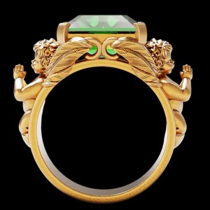Peut inclure: Une bague en or orn&eacute;e d'une grande pierre verte taill&eacute;e en &eacute;meraude. Deux ch&eacute;rubins aux bras tendus encadrent la gemme, avec des d&eacute;tails de plumes. La bague a une finition polie, sur fond noir.