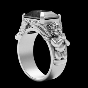 Peut inclure: Bague en argent orn&eacute;e d'une grosse pierre sombre. La conception de la bague comprend une figure d'ange et des accents de feuilles sur le bandeau, cr&eacute;ant un bijou unique et d&eacute;taill&eacute;.