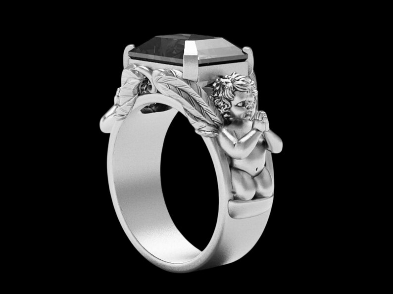 Peut inclure: Bague en argent orn&eacute;e d'une grosse pierre sombre. La conception de la bague comprend une figure d'ange et des accents de feuilles sur le bandeau, cr&eacute;ant un bijou unique et d&eacute;taill&eacute;.