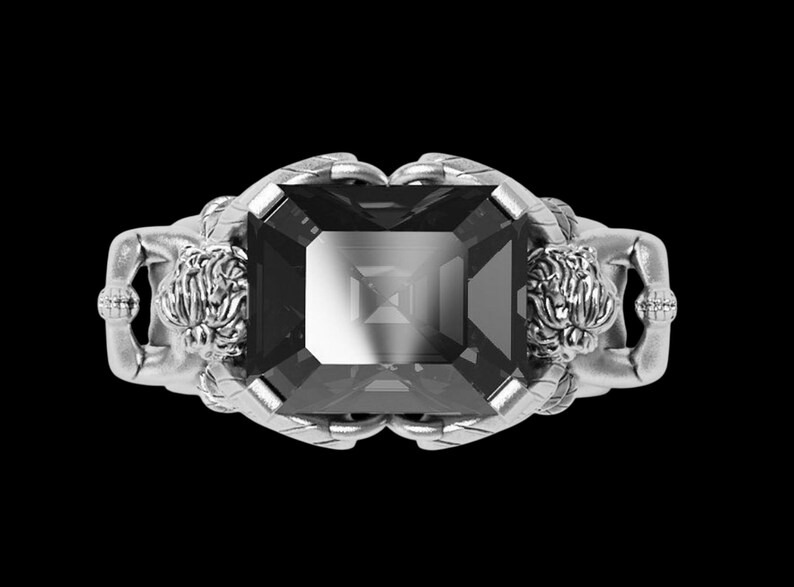Peut inclure: Bague en argent avec une grosse pierre pr&eacute;cieuse rectangulaire gris fonc&eacute;. La monture de la bague pr&eacute;sente deux figures sculpt&eacute;es tenant la pierre pr&eacute;cieuse. Les figures ont des cheveux d&eacute;taill&eacute;s et sont positionn&eacute;es de chaque c&ocirc;t&eacute; de la pierre.