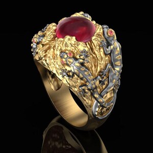Op de afbeelding: Een goudkleurige ring met een grote, ronde, rode edelsteen. De ring is versierd met getextureerde gouden details en verschillende kleine, zilver-zwarte gekko's met rode ogen. De ring heeft een gepolijste afwerking.