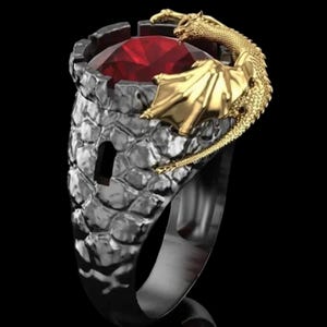 May include: A silver-toned ring featuring a castle-like setting with a large, red gemstone. A gold-colored dragon wraps around the setting. The ring has a textured surface and a dark band.