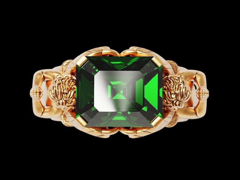 Peut inclure: Une bague en or avec une grosse pierre verte taill&eacute;e en &eacute;meraude. La bague pr&eacute;sente des d&eacute;tails dor&eacute;s orn&eacute;s, notamment des figures sculpt&eacute;es de chaque c&ocirc;t&eacute; de la pierre. Le fond est noir.