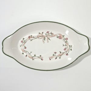 May include: Oval serving dish with a white base, a green rim, and a pink ribbon and floral design. The dish has a scalloped edge and is ideal for serving appetizers or desserts.