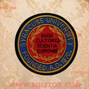 Puede incluir: Un parche bordado circular que presenta el sello de la Universidad de Syracuse. El diseño incluye un centro rojo con tallos de trigo dorados y el texto negro SUOS CULTORES SCIENTIA CORONAT, rodeado por un borde azul con el texto dorado SYRACUSE UNIVERSITY FOUNDED A.D. 1870.